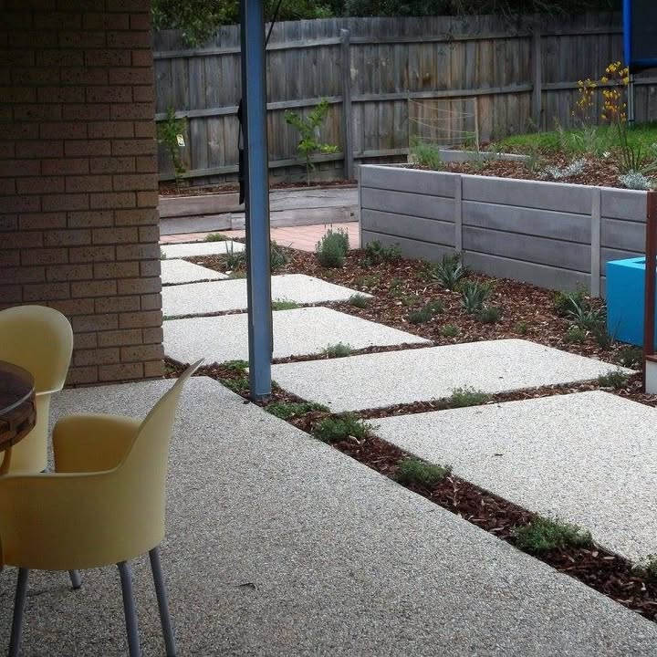 Exposed aggregate patio and stepping pads set into garden beds beside a concrete sleeper retaining wall