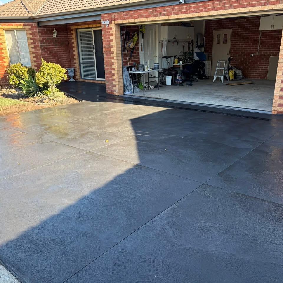 Dark charcoal stamped concrete driveway in a large-format tile pattern in front of a brick house