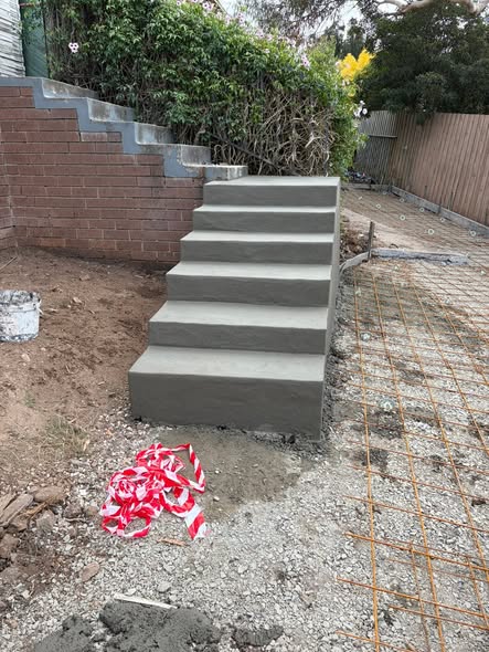 Freshly poured grey concrete steps against a brick retaining wall with construction tape still up