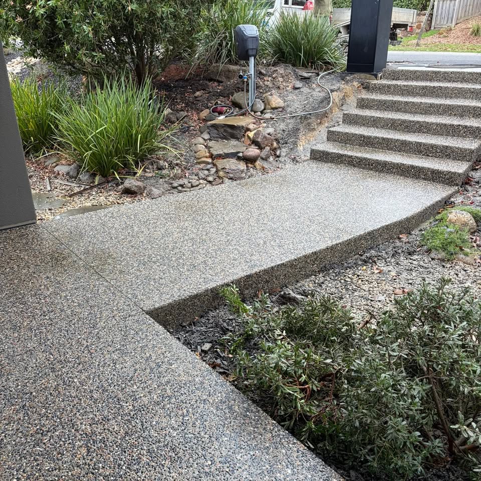 Exposed aggregate path and matching steps curving beside a modern home entrance
