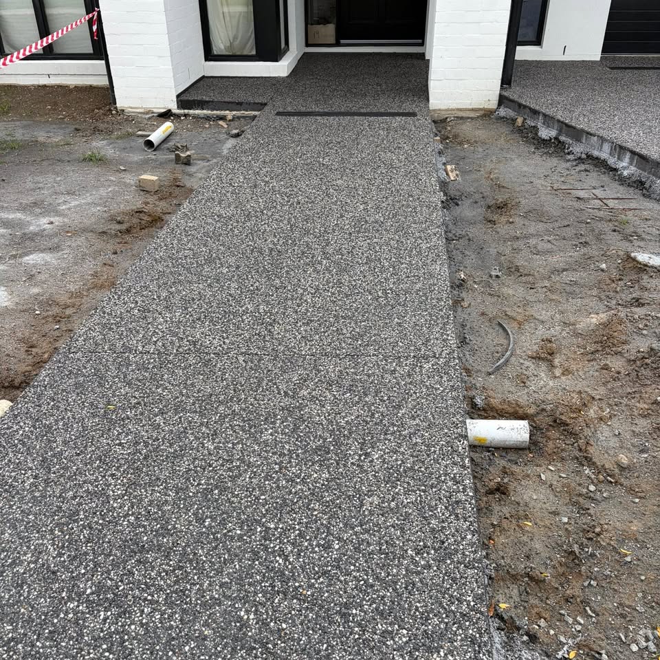 Broom-finished grey concrete path leading to the entrance of a newly built home